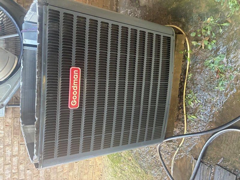 Performed a scheduled service agreement inspection on the Goodman outdoor condenser unit. Visually inspected the cabinet, louvered top grille, and condenser coil surfaces, which appeared clean and free of significant debris. Checked the interior base pan, compressor, copper refrigerant lines, and low-voltage wiring, and noted standing water in the base pan and saturated, muddy conditions around the pad, so drainage and moisture accumulation around the unit should be monitored.