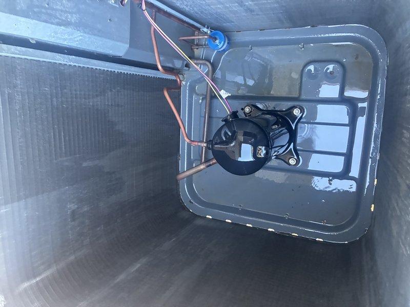 Performed a scheduled service agreement inspection on the Goodman outdoor condenser unit. Visually inspected the cabinet, louvered top grille, and condenser coil surfaces, which appeared clean and free of significant debris. Checked the interior base pan, compressor, copper refrigerant lines, and low-voltage wiring, and noted standing water in the base pan and saturated, muddy conditions around the pad, so drainage and moisture accumulation around the unit should be monitored.