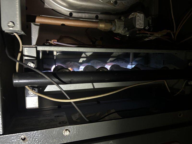 Performed scheduled maintenance inspection on the gas furnace and outdoor air conditioning condenser. Inspected the burner assembly, gas valve, supply piping, flame sensor/igniter, and wiring, and observed normal flame characteristics with some dust and discoloration noted on the burner area. Inspected the condenser unit, line set, conduit, and condensate drain, noting general weathering, dirt buildup, a peeling top label, and a slightly tilted, stained concrete pad.