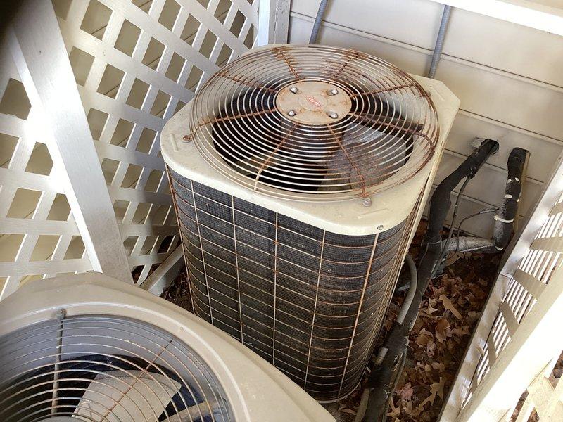 Conducted an estimate for replacement of an HVAC system serving the first and second floors with air handler located in garage. Inspected existing outdoor units housed within white lattice enclosure, noting aged condensers with visible wear and dirt accumulation on exterior fins.
