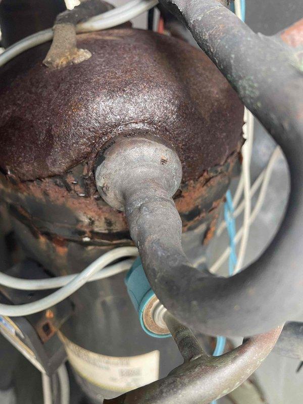 Responded to no heat complaint where tenant had reported frozen heat pump. Upon inspection, found severe corrosion on the reversing valve assembly affecting system operation. Placed unit in emergency heat mode as temporary solution while awaiting parts for permanent repair. Documented condition with photographs showing extensive rust damage to critical components.