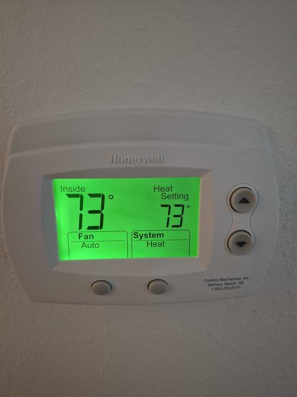 Performed routine heating system maintenance including electrical voltage testing on the outdoor unit (recorded 187V) and verified proper thermostat operation (Honeywell digital thermostat set to 73°F with "System: Heat" and "Fan: Auto" modes functioning correctly).