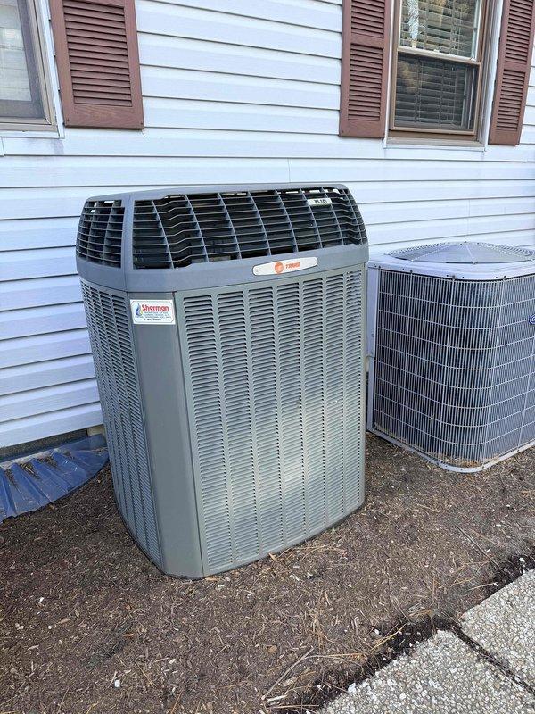 Conducted assessment of 15-year-old Trane heat pump system located in utility closet for potential replacement. Documented existing installation including indoor air handler in utility closet adjacent to Bradford White water heater with expansion tank. Exterior inspection revealed two outdoor units (primary Trane condenser and secondary unit) installed on ground level against vinyl siding, both appearing operational but at end of useful service life.