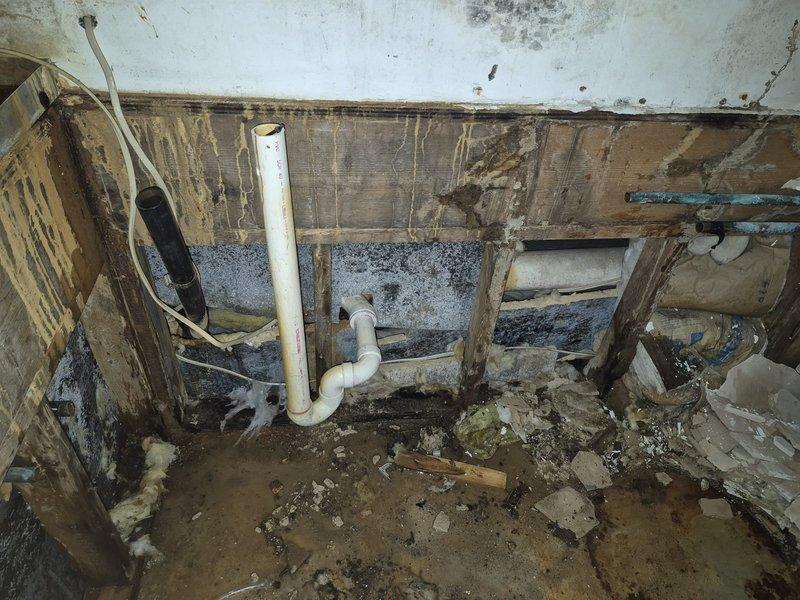 Responded to service call to disconnect water softener and water line. Upon inspection, discovered significant water damage to interior wall with exposed wooden framing showing deterioration and possible mold growth. Completed requested disconnection work and documented condition of the Rheem Classic water heater, which showed signs of surrounding moisture issues on the concrete floor and adjacent walls.