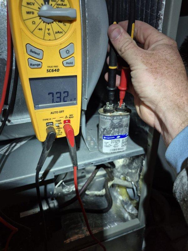 Performed routine cooling maintenance check on residential HVAC system. Conducted electrical diagnostics with multimeter on capacitor showing 732 reading. Observed significant rust/corrosion on compressor base plate and interior components requiring future attention.