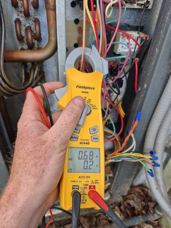 Performed inspection and cooling system check on hybrid HVAC unit. Verified electrical connections at contactor and control panel, measured refrigerant line amperage using clamp meter with readings of 0.68A and 0.2A, and inspected copper refrigerant lines which showed surface oxidation and corrosion buildup. Confirmed thermostat operation with Honeywell digital unit displaying 70°F indoor temperature and cooling mode engaged. Removed debris from unit interior and verified system operational parameters within acceptable range.