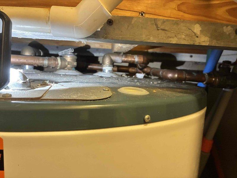 Performed on-site evaluation of 50-gallon electric water heater located in utility closet and assessed hall toilet reported to be leaking. Inspected existing water heater installation, noting age-related deterioration including mineral deposits and water staining on tank top, patina on copper supply lines, and overall condition of plumbing connections including brass fittings, shut-off valves, and temperature/pressure relief valve assembly. Documented current Rheem unit configuration with copper and PEX supply piping in confined space installation. Evaluated hall toilet for reported leak condition. Provided estimates for complete replacement of water heater unit and toilet fixture as requested by HOA requirements.