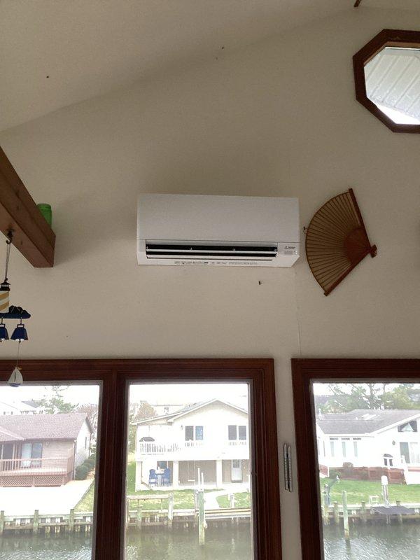 Installed Mitsubishi ductless mini-split system in back sun porch consisting of one MITMUZ-GX12NL 12,000 BTU 25 SEER outdoor heat pump unit and one MITMSZGX12NL 12,000 BTU wall-mounted indoor air handler with remote thermostat. Mounted indoor unit high on interior wall of vaulted ceiling room with waterfront view. Ran refrigeration lines concealed in slim duct chase down exterior side of home to outdoor condenser location. Coordinated with electrical contractor for dedicated circuit installation to support system requirements. Completed all refrigerant line connections, vacuum testing, and system charging per manufacturer specifications. Verified proper airflow, drainage, and operational performance of heating and cooling modes. Programmed remote thermostat and provided operational overview. System covered under one-year ductless warranty from installation date.