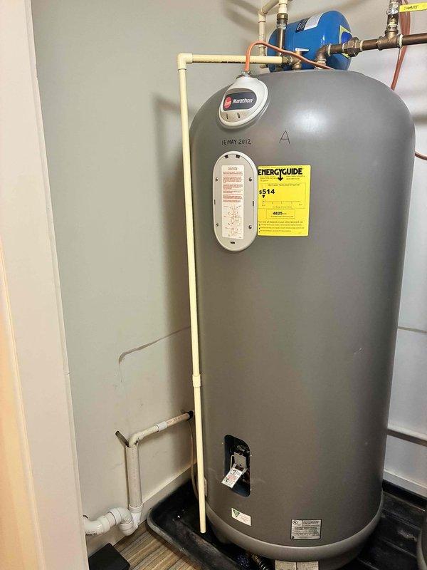 Completed installation of 50-gallon Rheem Marathon electric water heater, including filling tank and purging air from the system. During system startup and testing, discovered internal leak at bottom of existing 105-gallon Rheem Marathon tank (Model: MR10528, Serial: 0312W36790, manufactured May 2012). Determined tank failure is non-repairable internal defect requiring complete unit replacement. Documented equipment information and captured photographic evidence of failed unit for warranty verification purposes, including images of tank identification labels, plumbing connections, expansion tank, and overall system configuration.