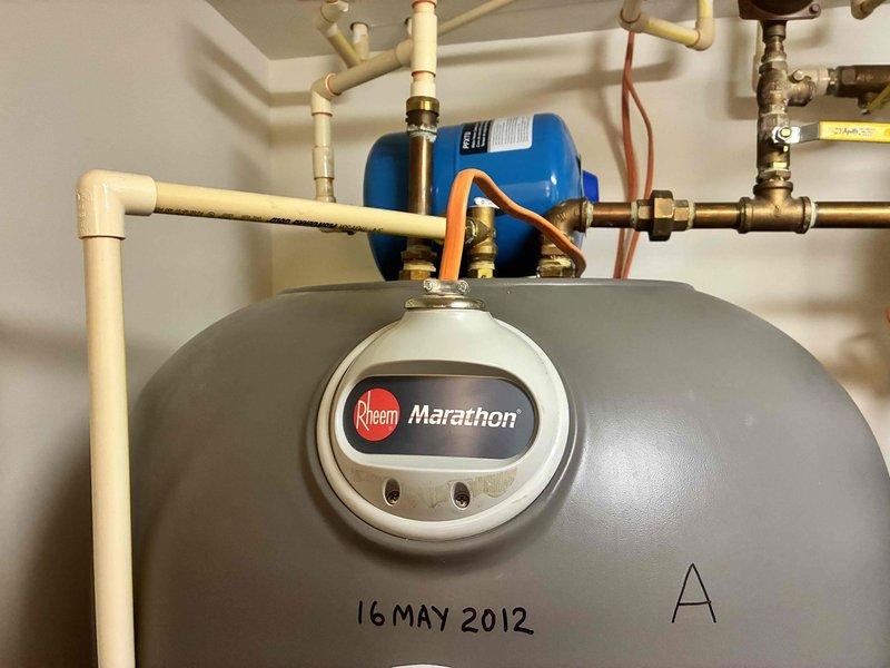 Completed installation of 50-gallon Rheem Marathon electric water heater, including filling tank and purging air from the system. During system startup and testing, discovered internal leak at bottom of existing 105-gallon Rheem Marathon tank (Model: MR10528, Serial: 0312W36790, manufactured May 2012). Determined tank failure is non-repairable internal defect requiring complete unit replacement. Documented equipment information and captured photographic evidence of failed unit for warranty verification purposes, including images of tank identification labels, plumbing connections, expansion tank, and overall system configuration.