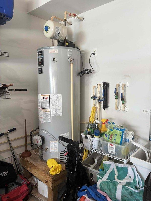 Performed on-site evaluation of existing 13-year-old 65-gallon gas-fired tank water heater located in garage. Inspected unit condition, venting system through exterior wall, copper supply line connections, and gas line configuration. Documented current installation including water treatment device, shut-off valves, and plumbing connections. Provided estimate for complete water heater replacement.