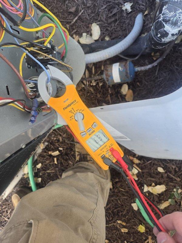 Performed routine cooling system maintenance on outdoor heat pump unit and verified electrical connections. Measured voltage at control board terminal block, recording 12.1V reading to confirm proper low-voltage power supply to unit controls. Inspected attic ductwork and recorded supply air temperature of 83.5°F at main trunk line. All electrical connections secure, unit operational, and system cooling properly.