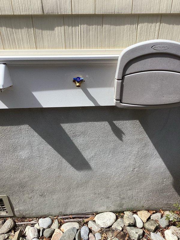Responded to service call for malfunctioning exterior hose bib (silcock) located on rear of structure. Inspected frost-free silcock mounted on shingled exterior wall and assessed associated shutoff valve on opposite side of building. Documented existing conditions of both plumbing fixtures with photographic evidence showing silcock installation above decorative rock landscaping and white PVC supply line configuration. Coordinated property access with homeowner for completion of necessary repairs to ensure proper water supply control and prevent potential freeze damage to exterior plumbing fixtures.