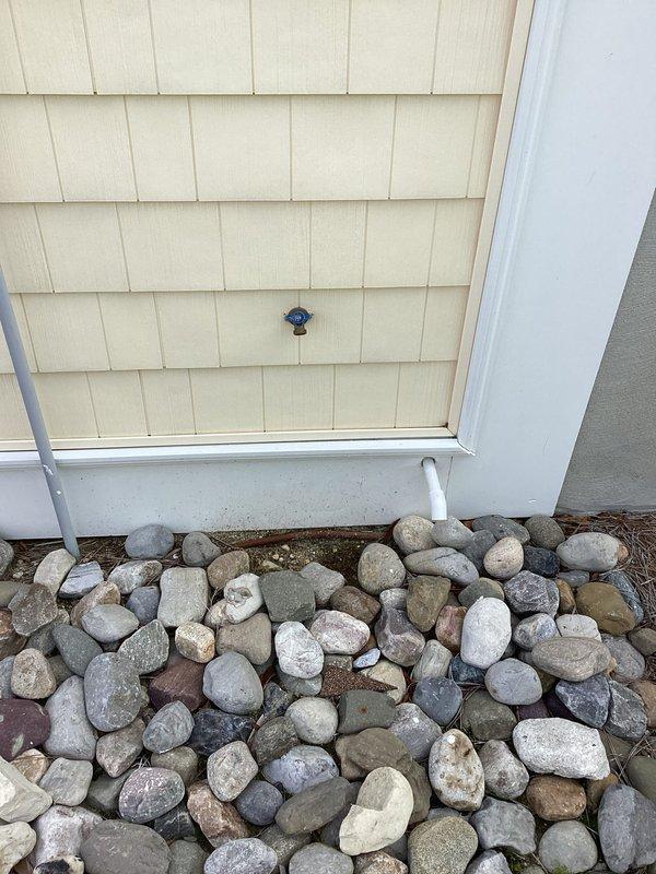 Responded to service call for malfunctioning exterior hose bib (silcock) located on rear of structure. Inspected frost-free silcock mounted on shingled exterior wall and assessed associated shutoff valve on opposite side of building. Documented existing conditions of both plumbing fixtures with photographic evidence showing silcock installation above decorative rock landscaping and white PVC supply line configuration. Coordinated property access with homeowner for completion of necessary repairs to ensure proper water supply control and prevent potential freeze damage to exterior plumbing fixtures.