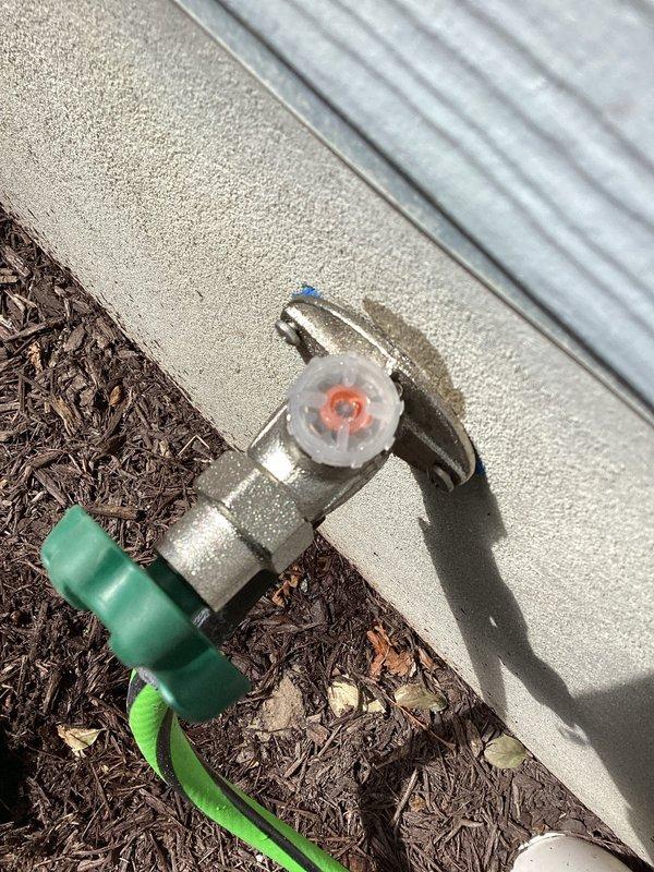 Responded to warranty callback for leaking hose bib on left side of building exterior that was recently installed. Upon inspection, identified leak at the outdoor spigot connection point. Accessed interior plumbing through utility room to diagnose source of water intrusion, which had caused visible moisture damage to vinyl plank flooring. Repaired faulty connection at the hose bib assembly, tested system for proper operation and verified no additional leaks present. Confirmed outdoor spigot now functioning correctly with green garden hose attached and no water discharge at mounting point or interior connections.
