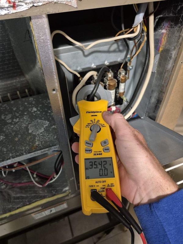 Responded to no heat call on system less than 10 years old that was running but failing to reach setpoint. Upon arrival, performed diagnostic testing using digital multimeter to measure system voltage and amperage. Initial voltage reading showed 35.42V at blower motor assembly, indicating potential low voltage issue. Further testing revealed amperage draw of 179.8A, which is significantly elevated and indicative of a locked rotor or failing motor condition. Inspected interior components including copper refrigerant lines, electrical connections, blower motor housing, and wiring harnesses. Found blower motor drawing excessive current while attempting to operate, causing system to run continuously without adequate air circulation to satisfy thermostat demand. The elevated amperage reading confirmed motor failure, preventing proper heat distribution throughout the space. Documented findings with photos showing diagnostic meter readings and internal equipment condition for service records.