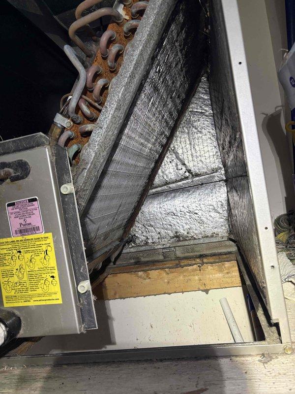 # HVAC Cooling System Maintenance

Performed routine cooling maintenance visit on residential air handler unit. Upon inspection, discovered evaporator coil assembly displaying moderate to heavy rust corrosion on copper refrigerant tubing, with orange-brown oxidation present throughout the coil structure. Coil fins remained structurally intact despite visible aging.

Identified significant dust and debris accumulation on evaporator coil surfaces and aluminum fins, with thick matted contamination restricting airflow through the heat exchanger. Documented condition of interior components including foil-faced insulation lining, drainage pan, and refrigerant line connections. Interior insulation showed age-related wear but remained functional. Drain pan exhibited minor staining consistent with normal condensate drainage patterns.

Photographed corroded copper tubing and heavily soiled coil sections for maintenance records. System components showed signs of extended service life with minimal