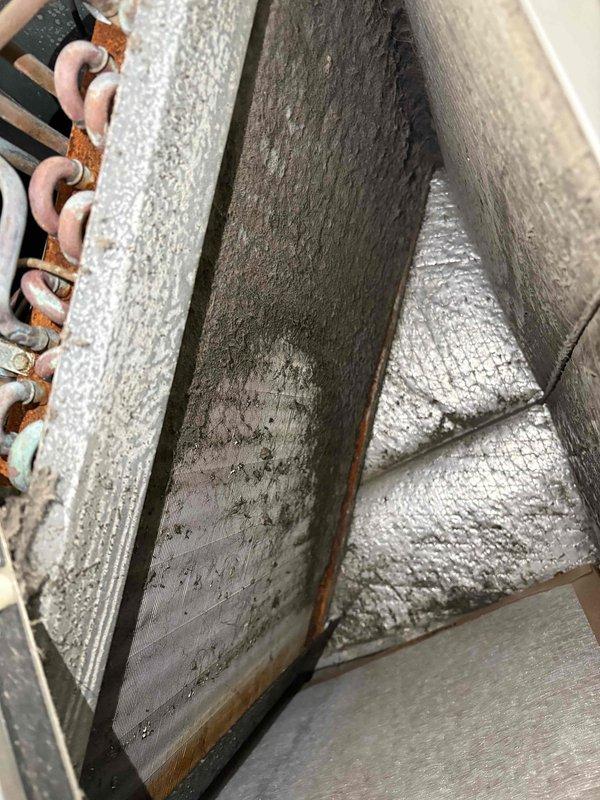 # HVAC Cooling System Maintenance

Performed routine cooling maintenance visit on residential air handler unit. Upon inspection, discovered evaporator coil assembly displaying moderate to heavy rust corrosion on copper refrigerant tubing, with orange-brown oxidation present throughout the coil structure. Coil fins remained structurally intact despite visible aging.

Identified significant dust and debris accumulation on evaporator coil surfaces and aluminum fins, with thick matted contamination restricting airflow through the heat exchanger. Documented condition of interior components including foil-faced insulation lining, drainage pan, and refrigerant line connections. Interior insulation showed age-related wear but remained functional. Drain pan exhibited minor staining consistent with normal condensate drainage patterns.

Photographed corroded copper tubing and heavily soiled coil sections for maintenance records. System components showed signs of extended service life with minimal