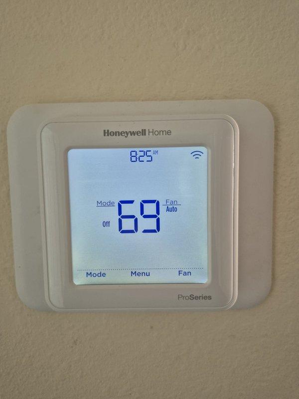 Performed cooling system maintenance and diagnostics on two HVAC units. Verified thermostat operation on Honeywell Home ProSeries unit displaying proper temperature readings and confirmed system settings in off mode with fan set to auto. Measured and recorded electrical voltage at 365V on system components using digital multimeter to ensure proper power supply to compressor and associated equipment.