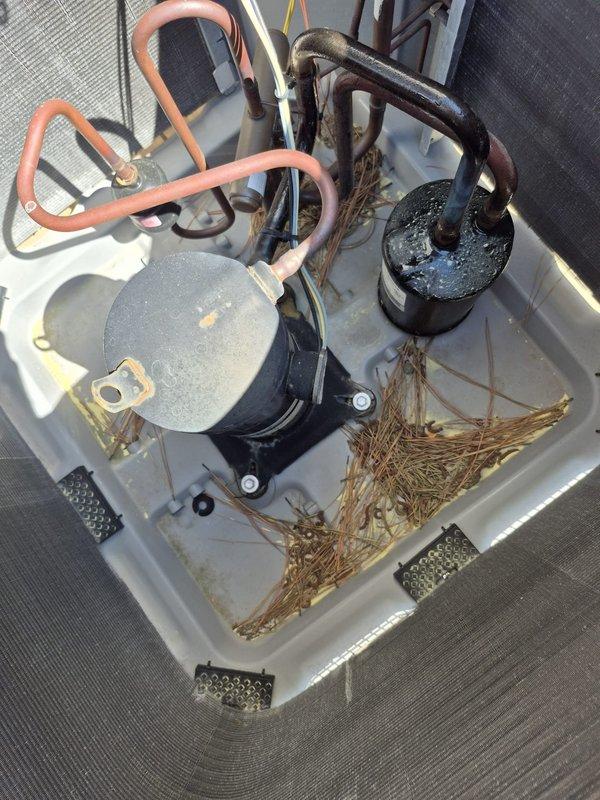 Performed routine cooling maintenance visit on dual HVAC system. Inspected rooftop equipment and removed significant accumulation of grass, straw, and organic debris from equipment pan and around compressor components to prevent airflow restrictions and potential system damage. Verified thermostat operation showing system cooling to setpoint of 74°F with unit running in auto fan mode at 27% capacity. Checked refrigerant line insulation and connections between compressor units, confirming proper installation and integrity of copper lines and foam insulation wrapping.