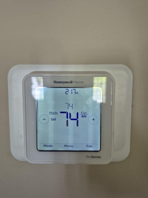 Performed routine cooling maintenance visit on dual HVAC system. Inspected rooftop equipment and removed significant accumulation of grass, straw, and organic debris from equipment pan and around compressor components to prevent airflow restrictions and potential system damage. Verified thermostat operation showing system cooling to setpoint of 74°F with unit running in auto fan mode at 27% capacity. Checked refrigerant line insulation and connections between compressor units, confirming proper installation and integrity of copper lines and foam insulation wrapping.