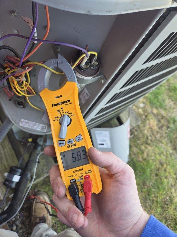 Performed cooling system maintenance and diagnostics on outdoor condensing unit. Measured electrical current draw at 5.03 amps using clamp meter on compressor circuit and verified dual-run capacitor connections. Checked supply air temperature at indoor unit, recording 67°F at the register. All electrical connections, wiring, and capacitor tested within normal operating parameters. System operating efficiently with no service concerns identified.