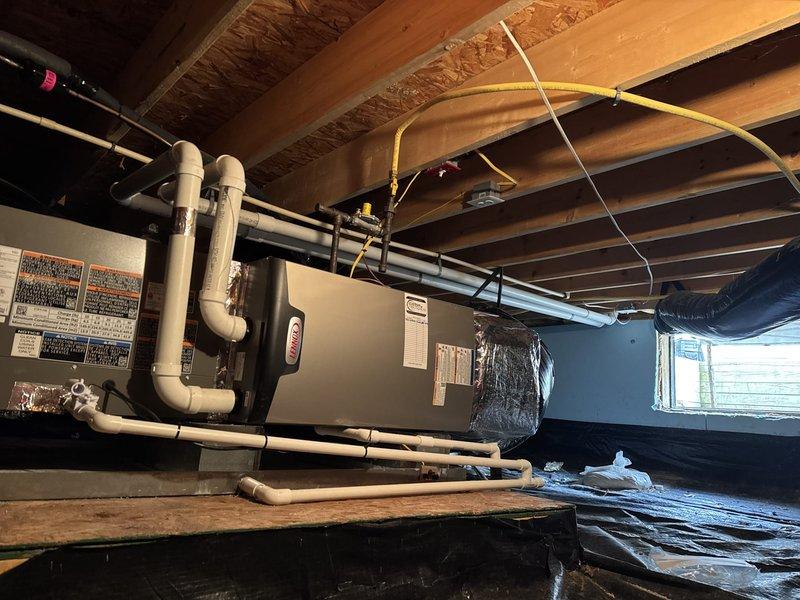 Completed full HVAC system replacement including removal and disposal of existing equipment. Installed Lennox EL297UH070E36 97% AFUE single-stage gas furnace with variable speed blower in basement crawl space. Mounted unit horizontally with proper condensate drainage using white PVC piping and connected yellow gas line. Fabricated and installed metal duct transitions to adapt new equipment to existing ductwork, with black insulated supply plenum visible in installation area.

Installed Lennox ML14KC1-042 3.5-ton 14 SEER air conditioner condenser unit on exterior of home. Positioned unit on pressure-treated wood platform for proper drainage and equipment protection. Replaced outdoor electrical disconnect and installed new electrical whip from junction box mounted on siding to condenser unit. Installed Lennox CK40DT-42B evaporator coil and LP conversion kit with furnace system.

Reused existing electrical service, condensate lines, and power supply connections where applicable to minimiz