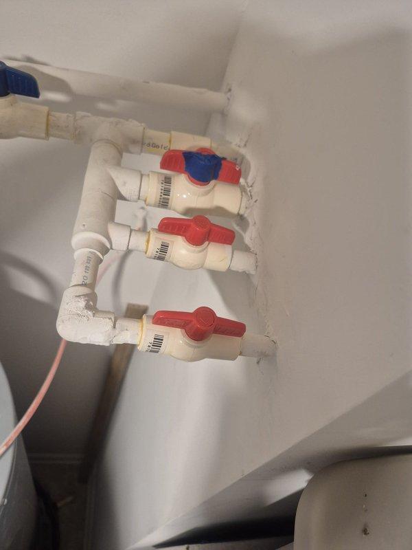 Conducted on-site assessment of existing main water shut-off valve system for replacement estimate. Evaluated current plumbing configuration consisting of multiple white PVC ball valves with color-coded handles (blue and red) mounted vertically on interior wall. Documented existing installation including valve condition, PVC piping connections, elbow joints, and overall system layout. Assessed white PEX supply lines with associated shut-off valves featuring red and blue handles and brass compression fittings. Photographed current plumbing infrastructure to provide accurate replacement specifications and scope of work for main shut-off valve replacement project.