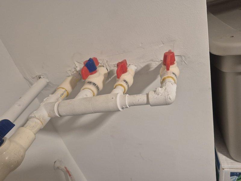 Conducted on-site assessment of existing main water shut-off valve system for replacement estimate. Evaluated current plumbing configuration consisting of multiple white PVC ball valves with color-coded handles (blue and red) mounted vertically on interior wall. Documented existing installation including valve condition, PVC piping connections, elbow joints, and overall system layout. Assessed white PEX supply lines with associated shut-off valves featuring red and blue handles and brass compression fittings. Photographed current plumbing infrastructure to provide accurate replacement specifications and scope of work for main shut-off valve replacement project.