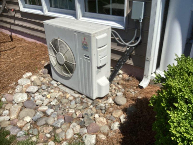 Performed site assessment and provided estimate for replacement of 19-year-old Mitsubishi mini-split system serving sunroom area. Documented existing outdoor condensing unit installation, electrical panel configuration with Square D breakers, and current system placement on gravel bed with proper clearances. Photographed equipment condition and electrical infrastructure to prepare comprehensive replacement proposal.