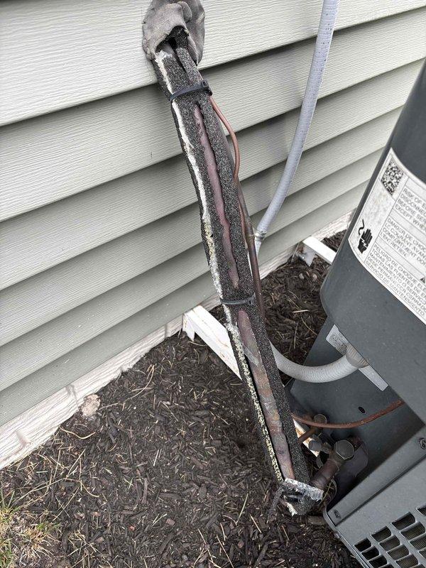 Responded to service call for outdoor HVAC unit experiencing operational noise and incomplete refrigerant line insulation per home inspection findings. Upon arrival, inspected condensing unit and discovered significant deterioration of black foam insulation on copper refrigerant lines, with extensive cracking, splitting, and gaps exposing bare copper tubing throughout the vertical run along exterior wall. Documented weathered and fragmented insulation condition showing age-related degradation. Evaluated unit operation and assessed noise complaint in conjunction with compromised line insulation. Photographed deteriorated insulation on refrigerant lines and overall system installation for documentation purposes.