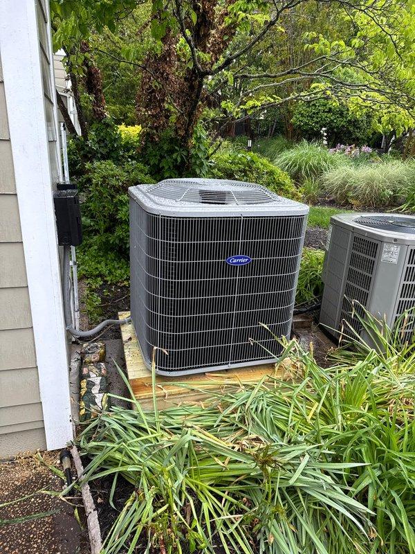 Completed full HVAC system replacement including removal and disposal of existing equipment. Installed new Carrier 27SCA524A003 2-ton 15 SEER heat pump on pressure-treated wood platform with Carrier FJ5ANXB24L00 air handler and 10kW electric heat pack in basement utility area. Fabricated and installed metal duct transitions to adapt new equipment to existing ductwork, reused existing condensate drain lines, replaced outdoor disconnect and electrical whip, and installed 14x24x1 filter grille and Honeywell TH6320WF digital WiFi thermostat for system control.