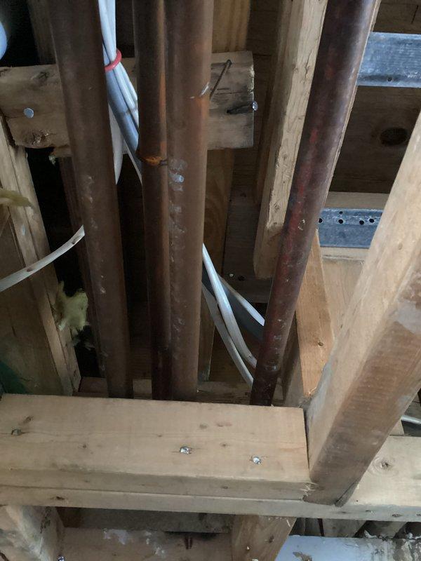 Conducted site assessment of existing plumbing infrastructure for kitchen renovation project involving relocation of water supply and drain lines into bay area. Inspected exposed framing cavity containing aged copper supply piping with significant oxidation and corrosion, existing PVC drain lines, and overhead joist space to determine feasibility of removing bulkhead and rerouting plumbing systems. Documented current pipe routing, structural constraints, and access points through framing members. Evaluated condition of existing copper piping, identified necessary tie-in locations for relocated fixtures, and assessed requirements for new supply risers, drain waste vent modifications, and potential need for pipe replacement due to deterioration. Photographed existing conditions including pipe runs through wall cavities and ceiling joists to develop scope of work and material requirements for kitchen plumbing relocation estimate.