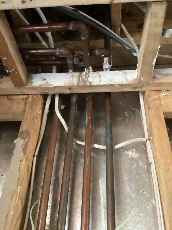 Conducted site assessment of existing plumbing infrastructure for kitchen renovation project involving relocation of water supply and drain lines into bay area. Inspected exposed framing cavity containing aged copper supply piping with significant oxidation and corrosion, existing PVC drain lines, and overhead joist space to determine feasibility of removing bulkhead and rerouting plumbing systems. Documented current pipe routing, structural constraints, and access points through framing members. Evaluated condition of existing copper piping, identified necessary tie-in locations for relocated fixtures, and assessed requirements for new supply risers, drain waste vent modifications, and potential need for pipe replacement due to deterioration. Photographed existing conditions including pipe runs through wall cavities and ceiling joists to develop scope of work and material requirements for kitchen plumbing relocation estimate.