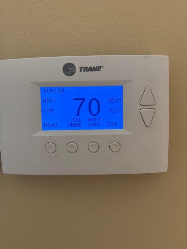 Performed seasonal cooling system maintenance check on HVAC unit. Upon arrival, disarmed security system as instructed and accessed property. Inspected Trane thermostat, which displayed proper operation in cooling mode with current settings at 70°F and programmed cooling setpoint at 72°F. Unit showed "WAIT" status indicating normal delay cycle protection. Examined triangular ceiling vent opening and noted significant accumulation of dust, dirt, and discoloration on mesh screen surrounding the black spiral ventilation duct. Documented conditions with photos showing staining and debris buildup around vent perimeter, which may impact air quality and system efficiency. Verified thermostat functionality and confirmed system responding appropriately to cooling demands. Rearmed security system upon completion of inspection.