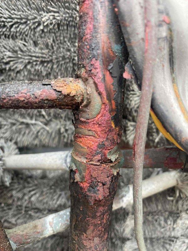 Responded to no cooling call on top floor unit. Upon inspection, discovered severe corrosion on refrigerant line connections at the outdoor condensing unit, causing refrigerant leak and loss of system charge. The corroded pipe joints showed extensive rust degradation and flaking at connection points, compromising system integrity. Documented equipment condition with photos showing the elevated condensing unit installation and deteriorated piping requiring immediate attention to restore cooling function.