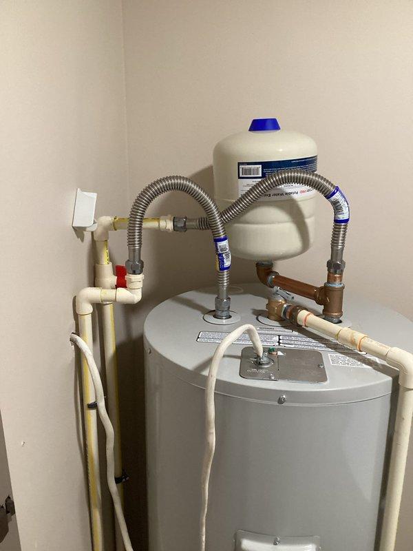 Successfully installed a 50-gallon tall residential electric water heater (model RE250T61) in a utility closet. Installation included a 22-inch drain pan positioned beneath the unit, a white expansion tank with blue cap mounted on top and connected via stainless steel braided flex connectors, and all necessary brass fittings including 3/4" nipples (2" and 6"), 90-degree elbow, and tee fitting. Connected hot and cold water supply lines using 18-inch flexible connectors, installed pressure relief valve with proper discharge piping, and ensured all electrical connections were properly secured. All plumbing connections were tested for leaks and the unit was verified operational upon completion.