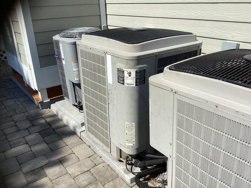 Completed HVAC system replacement including installation of three outdoor condensing units positioned on paver stone pad with proper spacing and mounting. Replaced indoor Bryant furnace system with new two-compartment unit, installed flexible ductwork with reflective insulation, and completed all necessary electrical conduit and wiring connections. All equipment photographed and documented upon completion.