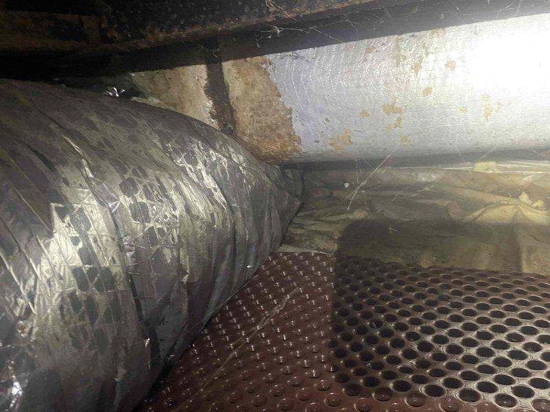 Responded to no cooling complaint on residential HVAC system. Upon inspection, accessed crawl space and evaluated ductwork system and structural conditions. Found flexible ductwork with visible deterioration including discolored tape connections and potential contamination on duct wrap material. Observed significant moisture damage to surrounding wooden structural members with advanced weathering and degradation. Documented conditions showing compromised crawl space environment with aged insulation, corroded piping, and moisture barrier flooring. Advised customer of findings and explained billing parameters for related versus unrelated repairs to original service call.