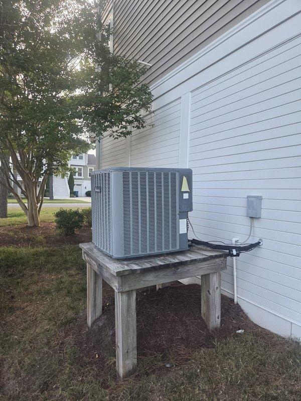 Responded to emergency no-cooling call for residential HVAC system over 10 years old. Upon arrival, found smart thermostat calling for cooling with setpoint of 70°F while indoor temperature reading showed 75°F and 45% humidity. Inspected outdoor condensing unit located on wooden platform adjacent to house with proper electrical disconnect and refrigerant line connections present. Documented system configuration and current operating conditions through diagnostic photography of both indoor thermostat display and outdoor equipment installation.