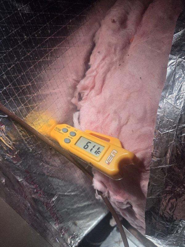 Responded to no cooling complaint on residential HVAC system less than 10 years old. Performed diagnostic testing in attic space using digital multimeter, obtaining temperature readings of 64.1°F at ductwork and insulation areas. Measurements taken at supply duct insulation and surrounding mechanical components to assess system performance and identify cooling deficiency cause.