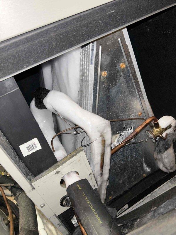 Responded to emergency no-cooling call and performed diagnostic inspection of air handler unit located in attic space. Upon arrival, accessed interior compartment to evaluate system components including evaporator coil, refrigerant lines, and condensate drainage system. Inspected copper refrigerant line connections with brass fittings, verifying proper installation and checking for visible signs of refrigerant leaks or damaged insulation. Examined evaporator coil fins for debris accumulation, blockage, or damage that could restrict airflow. Assessed condensate drain line configuration including PVC piping and elbow connections for proper drainage flow. Documented current condition of unit interior showing operational wear, dust accumulation on surfaces, and general equipment status. Photographed key system components including heat exchanger surfaces, refrigerant line routing, and access panel interior for service records. System age could not be determined from available manufacturer 