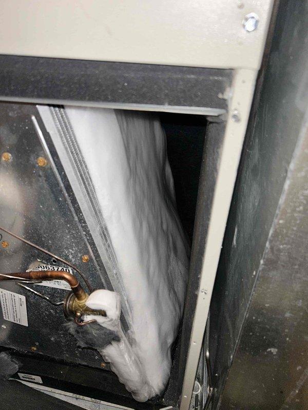 Responded to emergency no-cooling call and performed diagnostic inspection of air handler unit located in attic space. Upon arrival, accessed interior compartment to evaluate system components including evaporator coil, refrigerant lines, and condensate drainage system. Inspected copper refrigerant line connections with brass fittings, verifying proper installation and checking for visible signs of refrigerant leaks or damaged insulation. Examined evaporator coil fins for debris accumulation, blockage, or damage that could restrict airflow. Assessed condensate drain line configuration including PVC piping and elbow connections for proper drainage flow. Documented current condition of unit interior showing operational wear, dust accumulation on surfaces, and general equipment status. Photographed key system components including heat exchanger surfaces, refrigerant line routing, and access panel interior for service records. System age could not be determined from available manufacturer 
