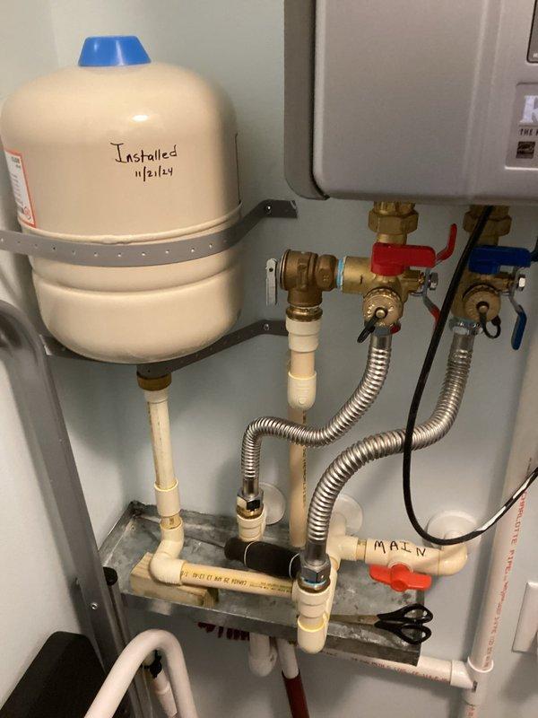 Responded to service call for Rinnai tankless water heater experiencing beeping alarm and complete loss of hot water. Upon inspection, determined the 2013 unit had reached end of service life and required full replacement. Installed new tankless water heater system with proper venting through white PVC exhaust assembly, including curved elbow connections and wall-mounted termination. Completed installation of expansion tank with pressure relief components, integrated main water line connections with brass shut-off valves for both hot and cold supply lines, and installed flexible connector hoses for proper system operation. All plumbing connections tested and verified leak-free, unit operational and providing hot water upon completion.