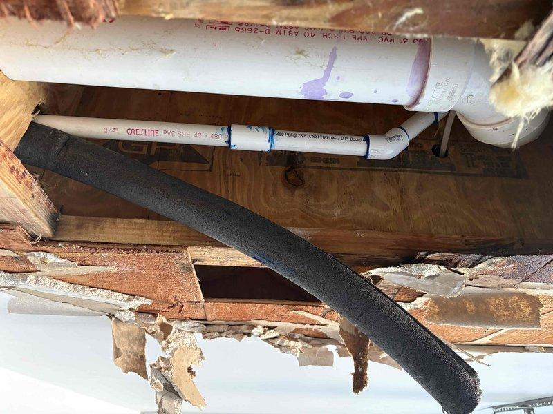 Responded to service call for AC unit backup that caused water damage and ceiling collapse. Inspected drain line system and photographed overhead plumbing infrastructure showing compromised drain pan and deteriorated structural materials around HVAC condensate drainage. Identified blockage in condensate drain line that caused water overflow into ceiling cavity. Assessed damaged building materials and insulation resulting from water intrusion. Recommended complete drain line cleaning and repair to prevent future backups.