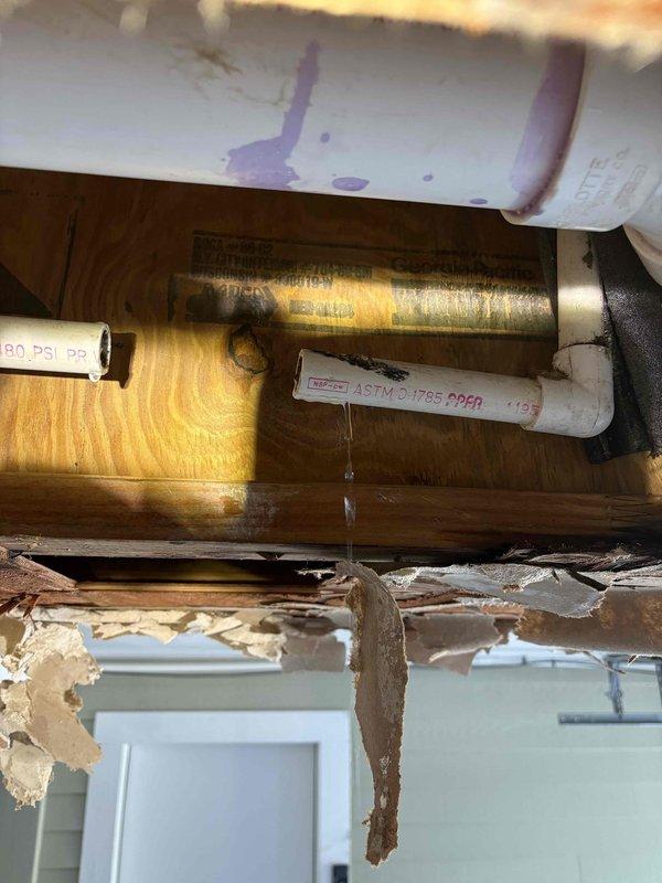 Responded to service call for AC unit backup that caused water damage and ceiling collapse. Inspected drain line system and photographed overhead plumbing infrastructure showing compromised drain pan and deteriorated structural materials around HVAC condensate drainage. Identified blockage in condensate drain line that caused water overflow into ceiling cavity. Assessed damaged building materials and insulation resulting from water intrusion. Recommended complete drain line cleaning and repair to prevent future backups.