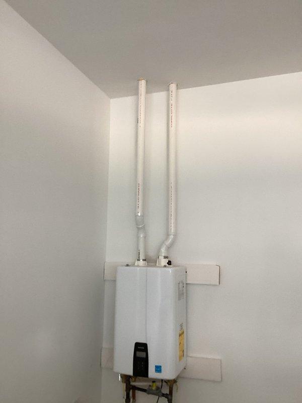 Responded to customer concern regarding watery, burning eyes potentially related to tankless gas water heater venting system. Performed comprehensive inspection of PVC venting pipes extending from unit through attic space to identify possible exhaust gas leakage or improper venting conditions. Examined all pipe connections, joints, and seals at the wall-mounted tankless water heater unit where dual white PVC intake and exhaust pipes connect. Verified proper installation of venting system, checked for separation at elbows and connection points, and assessed overall integrity of the venting pathway. Inspected copper water supply lines and electrical connections at unit base. Documented installation configuration with photographs for service records and customer reference.