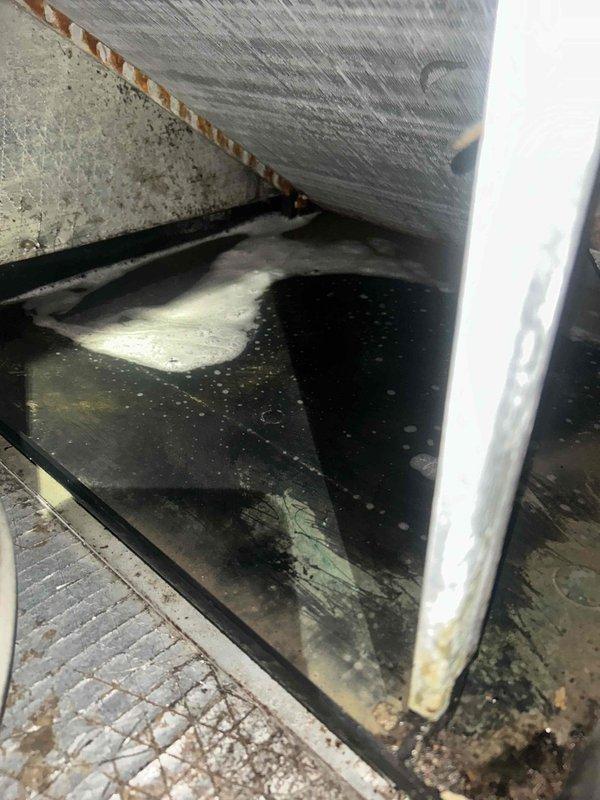 # HVAC Cooling System Maintenance Visit

Performed routine cooling maintenance inspection on residential air conditioning system. Upon accessing the unit's interior, discovered significant standing water accumulation in the condensate drain pan with visible debris, sediment, and particulate matter throughout. The drain pan exhibited extensive staining and discoloration, indicating prolonged moisture exposure and potential biological growth concerns.

Documented conditions of the evaporator coil assembly area, noting the quilted insulation material surrounding ductwork and refrigerant lines appeared intact. Copper fasteners securing insulation to metallic surfaces were properly positioned. However, the drain pan surface showed irregular black and dark brown staining patterns across the collection area, suggesting inadequate drainage or clogged condensate line requiring attention.

The unit's base cabinet interior revealed stagnant water conditions with accumulated organic debris that co
