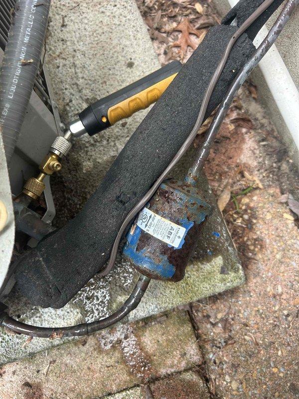 # HVAC Service Report

Responded to no cooling complaint on residential air conditioning system less than 10 years old. Upon arrival, performed visual inspection of outdoor condenser unit and associated components. Located system installed on paver stone patio area with dual condenser configuration against exterior wall.

Connected manifold gauge set to refrigerant service ports to assess system pressures and refrigerant charge levels. Gauges indicated abnormal pressure readings consistent with low refrigerant charge. Conducted thorough leak detection inspection of refrigerant lines, connections, and condenser coil. Identified refrigerant leak at service port connection on liquid line. Repaired leak by tightening connection and replacing service port cap.

Evacuated system to remove air and moisture from refrigerant circuit. Recharged system to manufacturer specifications using proper refrigerant type. Verified correct operating pressures on both high and low sides of system. Monitored
