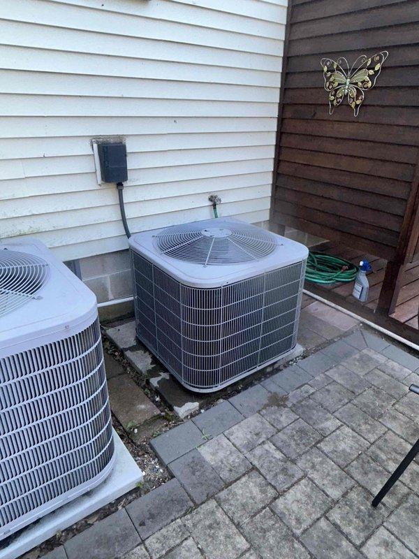 # HVAC Service Report

Responded to no cooling complaint on residential air conditioning system less than 10 years old. Upon arrival, performed visual inspection of outdoor condenser unit and associated components. Located system installed on paver stone patio area with dual condenser configuration against exterior wall.

Connected manifold gauge set to refrigerant service ports to assess system pressures and refrigerant charge levels. Gauges indicated abnormal pressure readings consistent with low refrigerant charge. Conducted thorough leak detection inspection of refrigerant lines, connections, and condenser coil. Identified refrigerant leak at service port connection on liquid line. Repaired leak by tightening connection and replacing service port cap.

Evacuated system to remove air and moisture from refrigerant circuit. Recharged system to manufacturer specifications using proper refrigerant type. Verified correct operating pressures on both high and low sides of system. Monitored